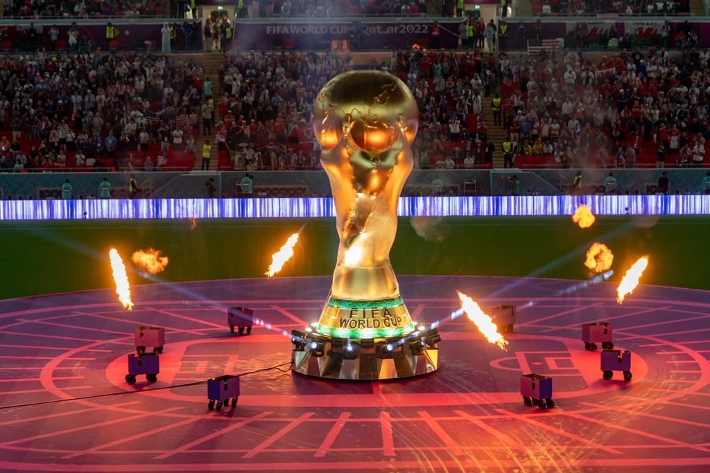 FIFA World Cup trophy displayed at the center of a packed stadium in Doha, with bright lights, cheering fans, and a dramatic match-day atmosphere in the background