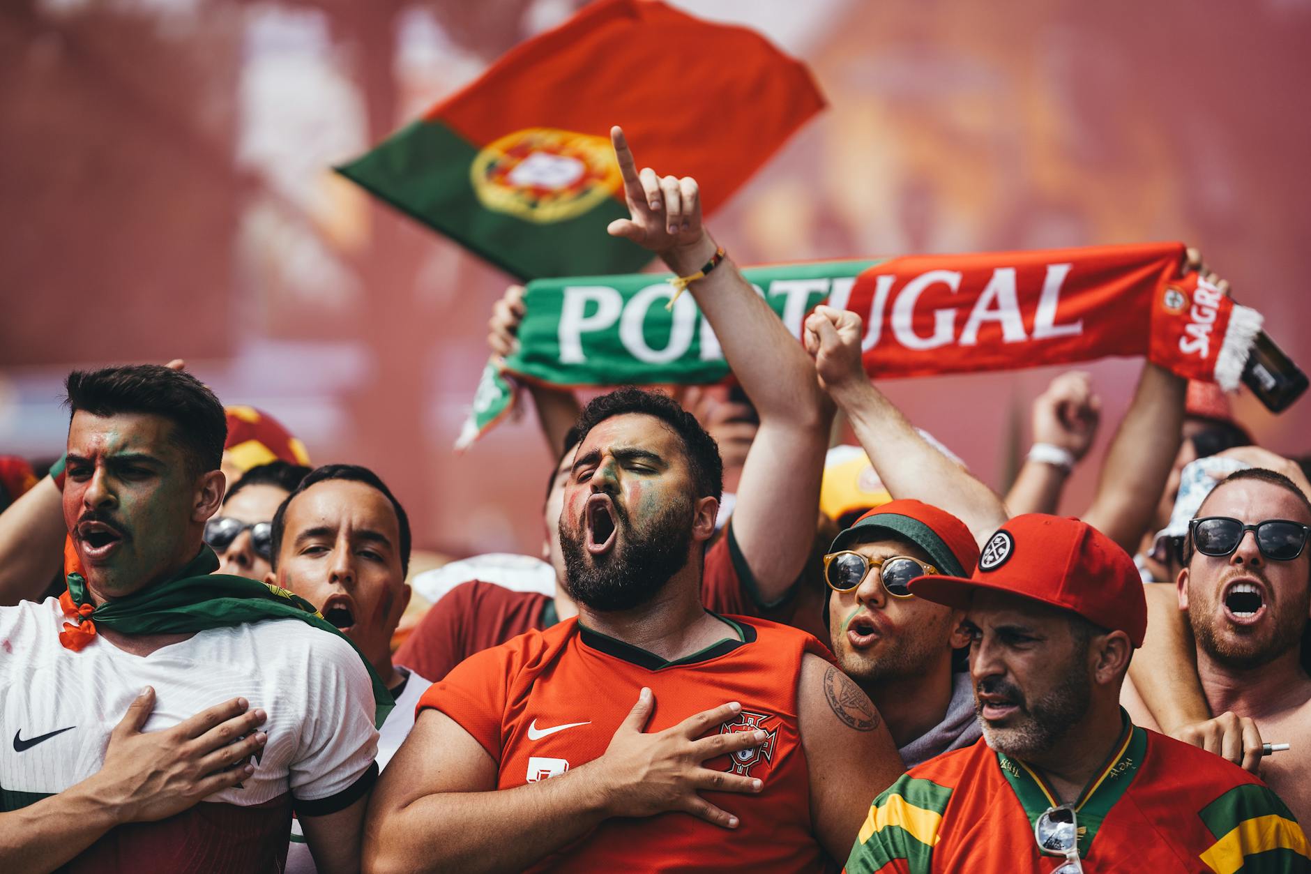 Portugal football fans waving flags and cheering in stadium stands during a World Cup match, wearing red and green team colors and celebrating passionately