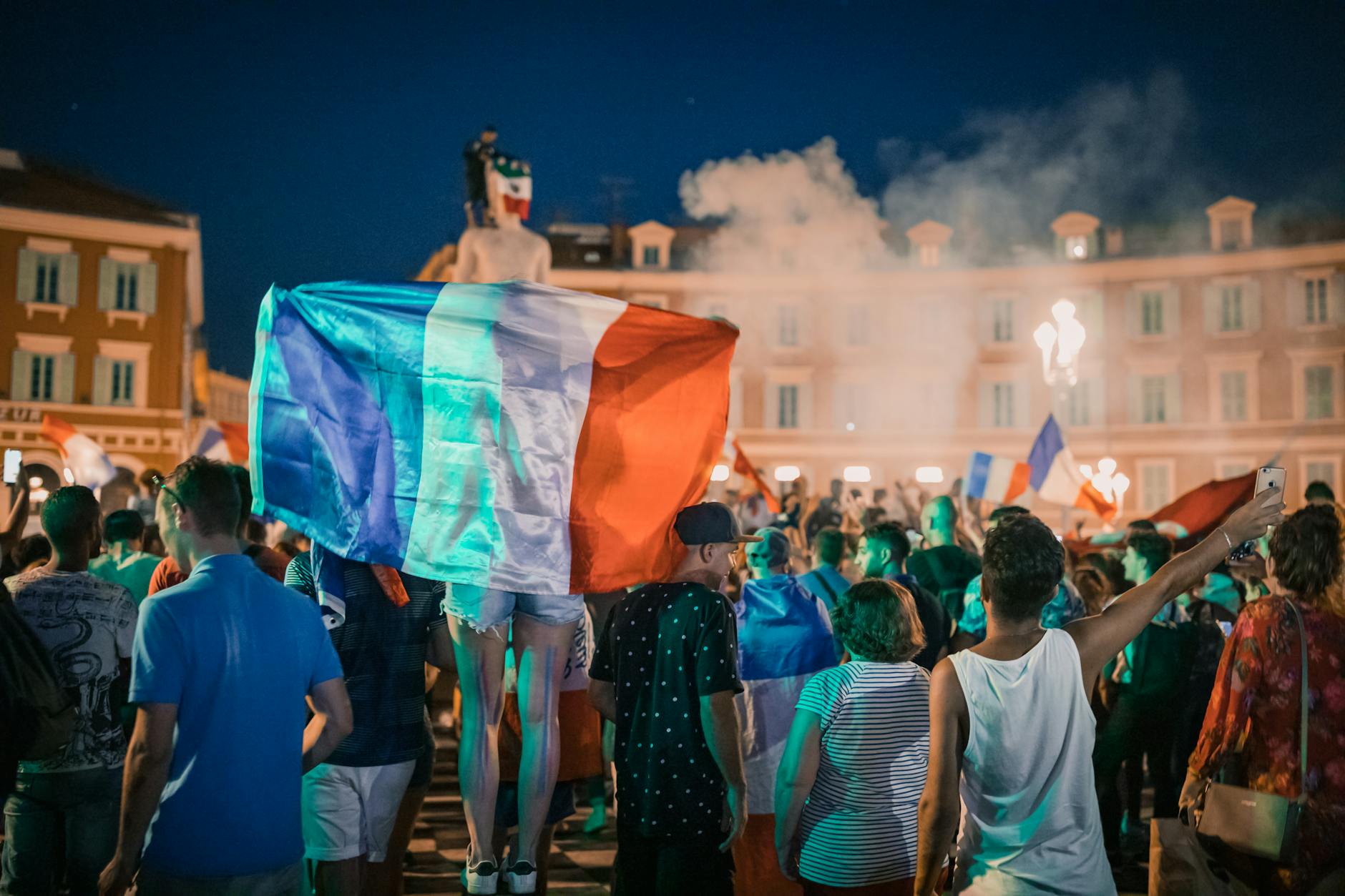 French football fans celebrating a FIFA World Cup victory, waving flags and lighting flares, with crowds cheering in the streets of Paris and a festive, electric atmosphere all around
